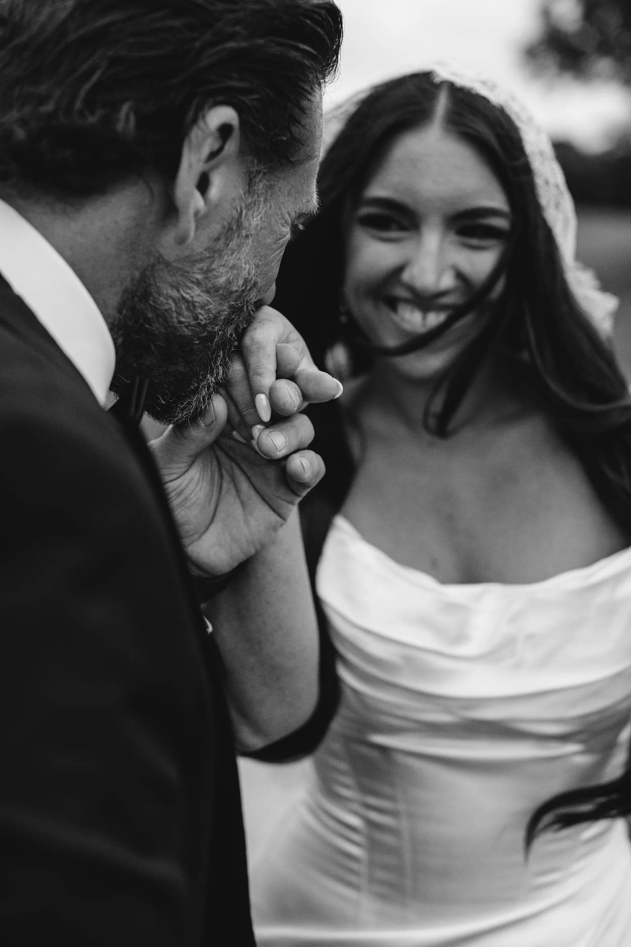 Black and white photo of a groom kissing his laughing bride's hand
