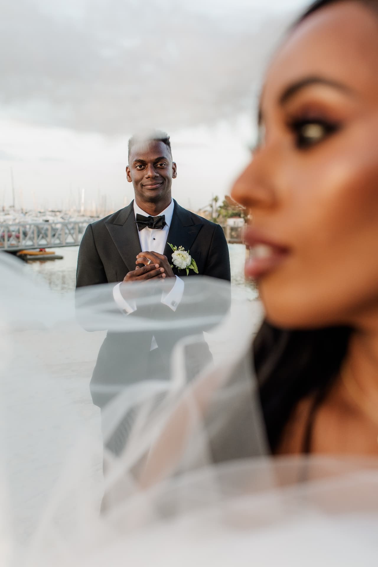 Artistic waterfront portrait of a groom seen through his bride's veil