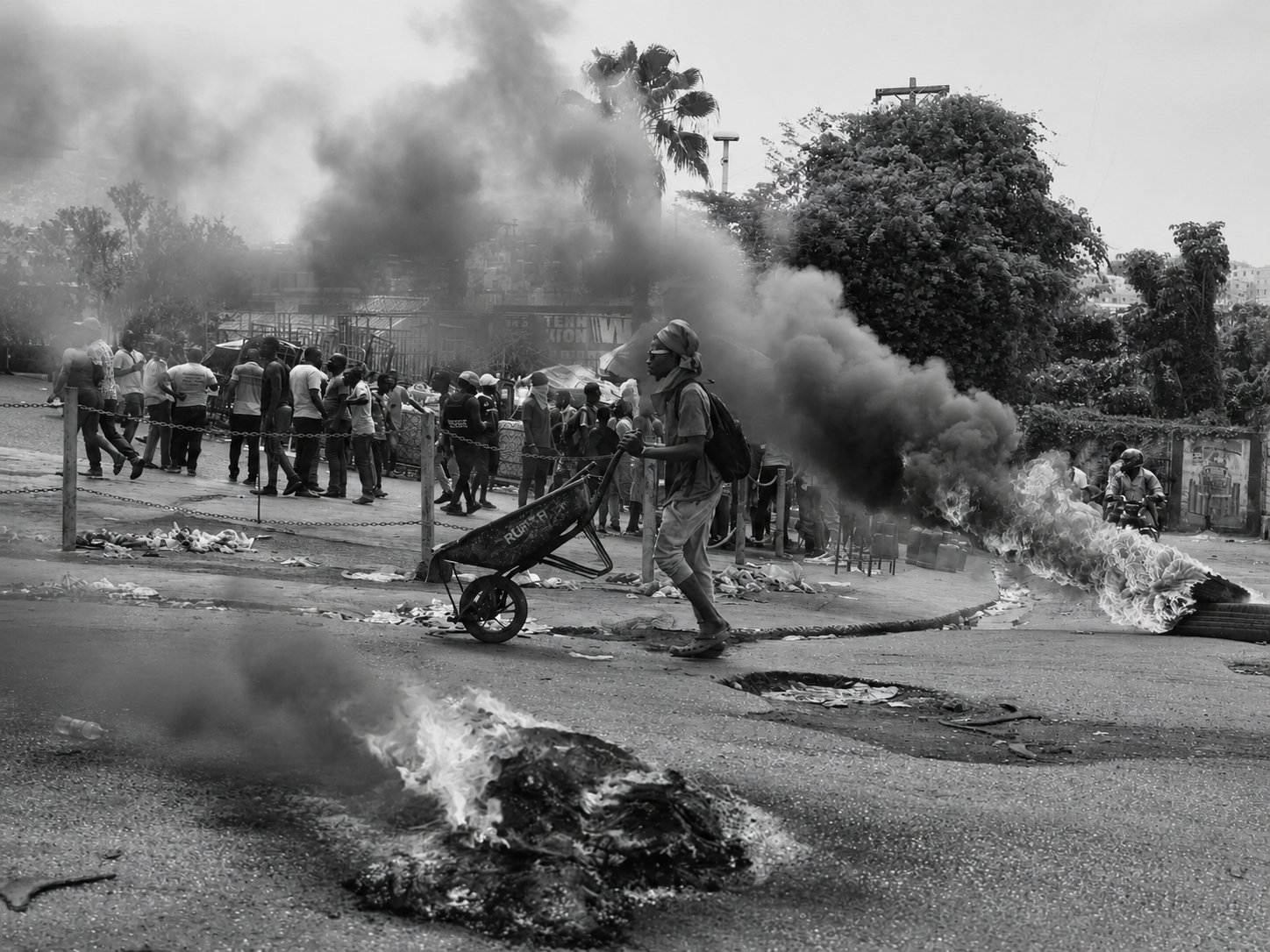 Documentary photograph from Haiti of a man pushing a wheelbarrow past burning debris