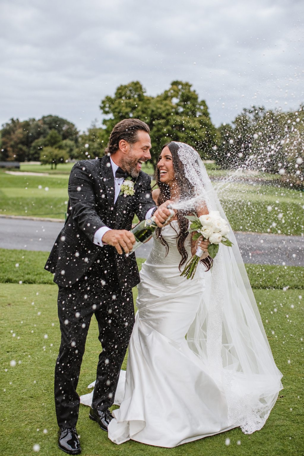 Bride and groom laughing as they spray champagne