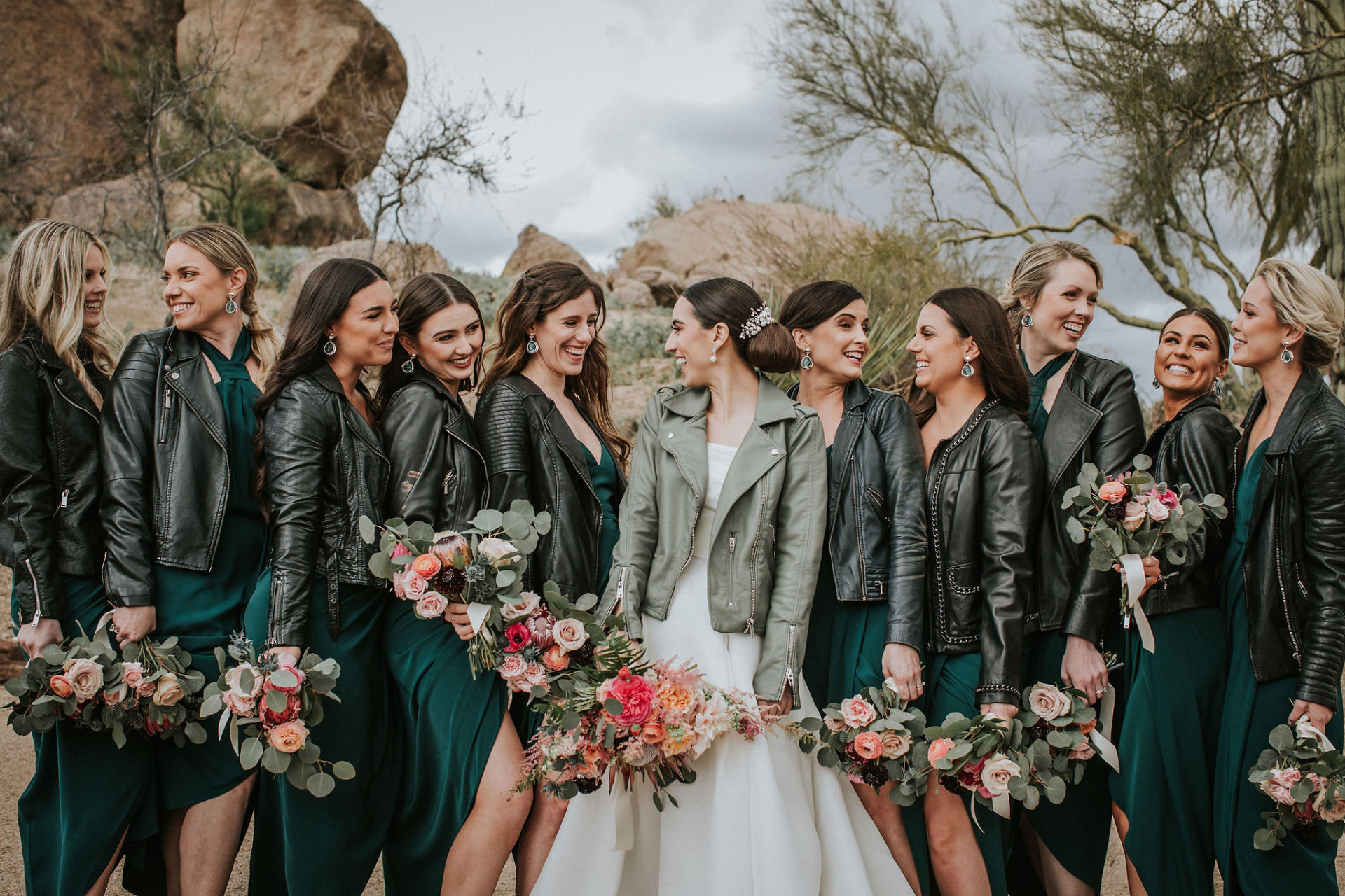 Bride laughing with bridesmaids in leather jackets in the desert