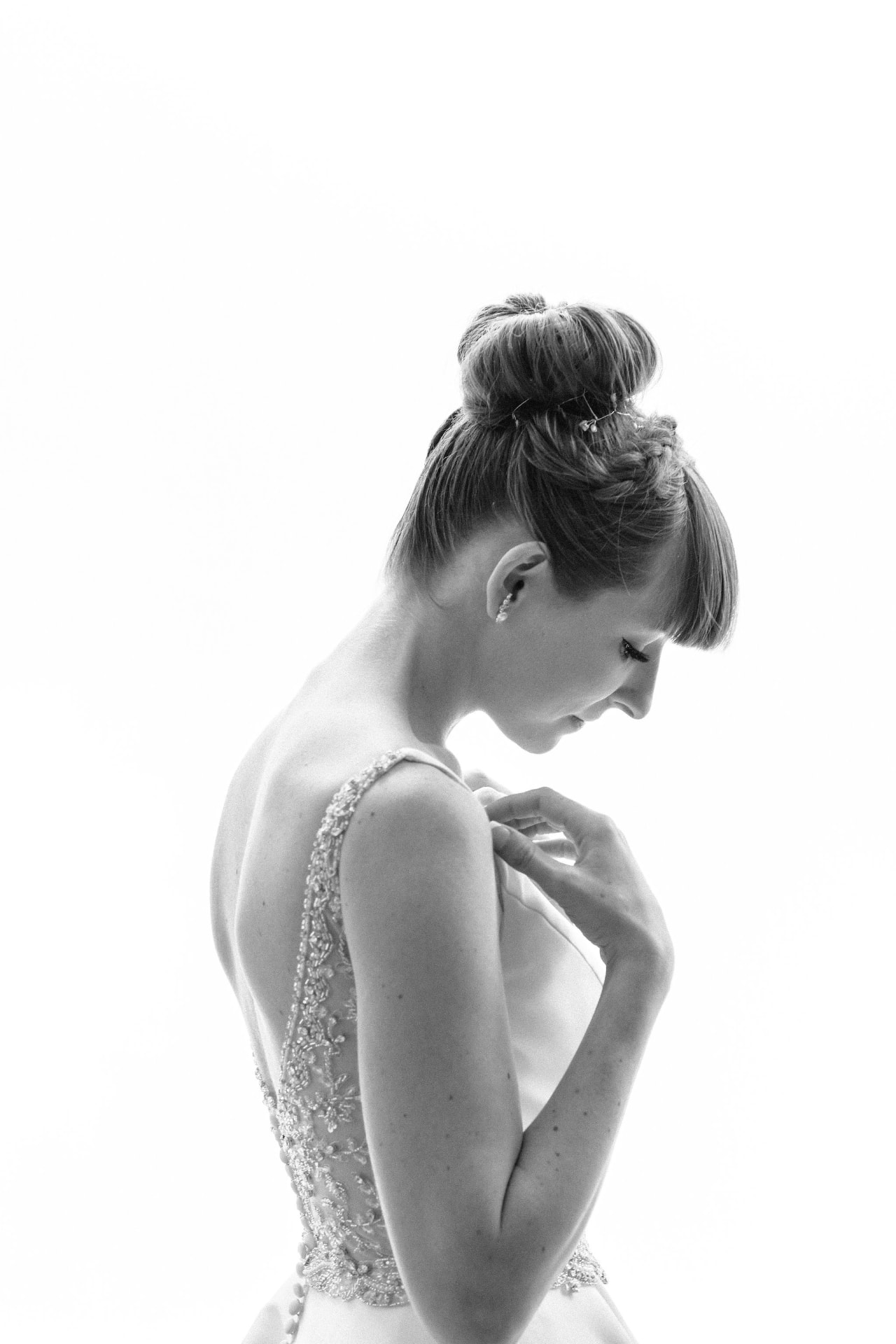 Black and white portrait of a bride fastening her beaded gown