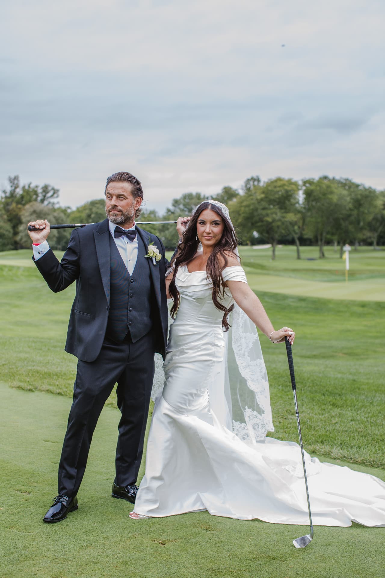 Bride and groom posing with golf clubs on the course