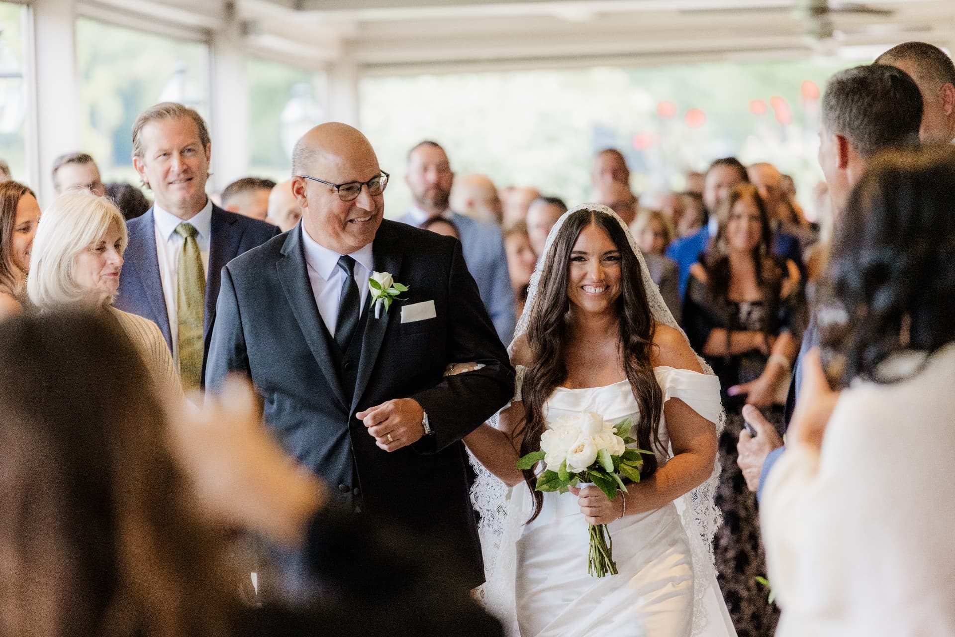 Smiling bride walking down the aisle arm in arm with her father as guests look on