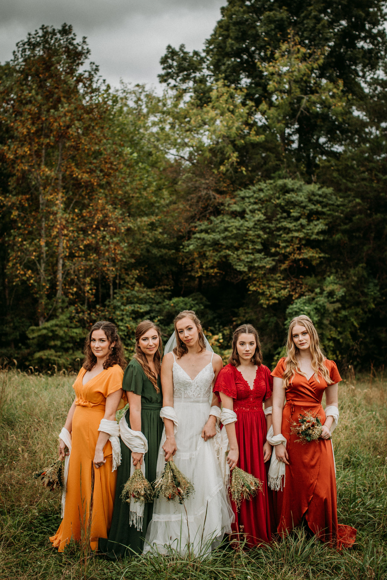 Bride and bridesmaids in autumn-toned dresses standing in a meadow