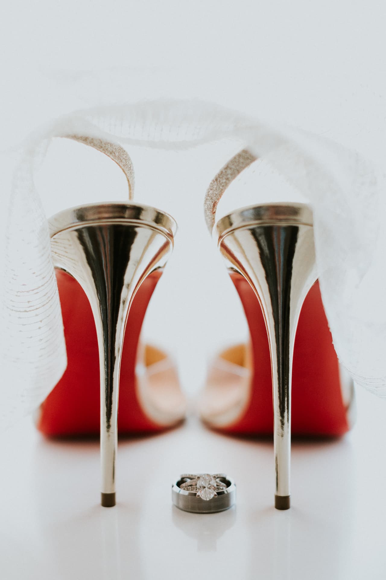 Bridal heels and wedding rings styled beside a delicate veil