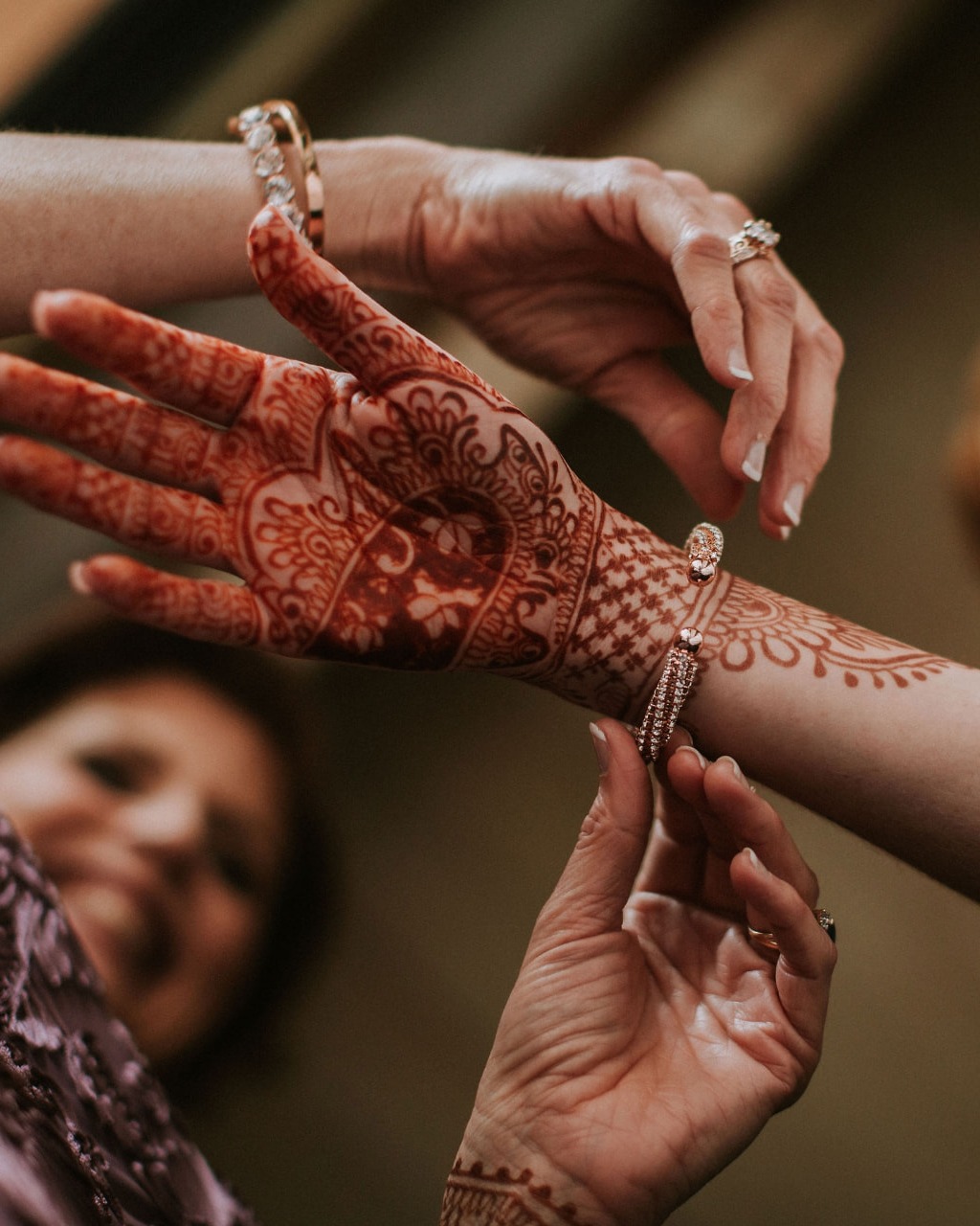 Intricate henna hands being adorned with jewelry before the wedding