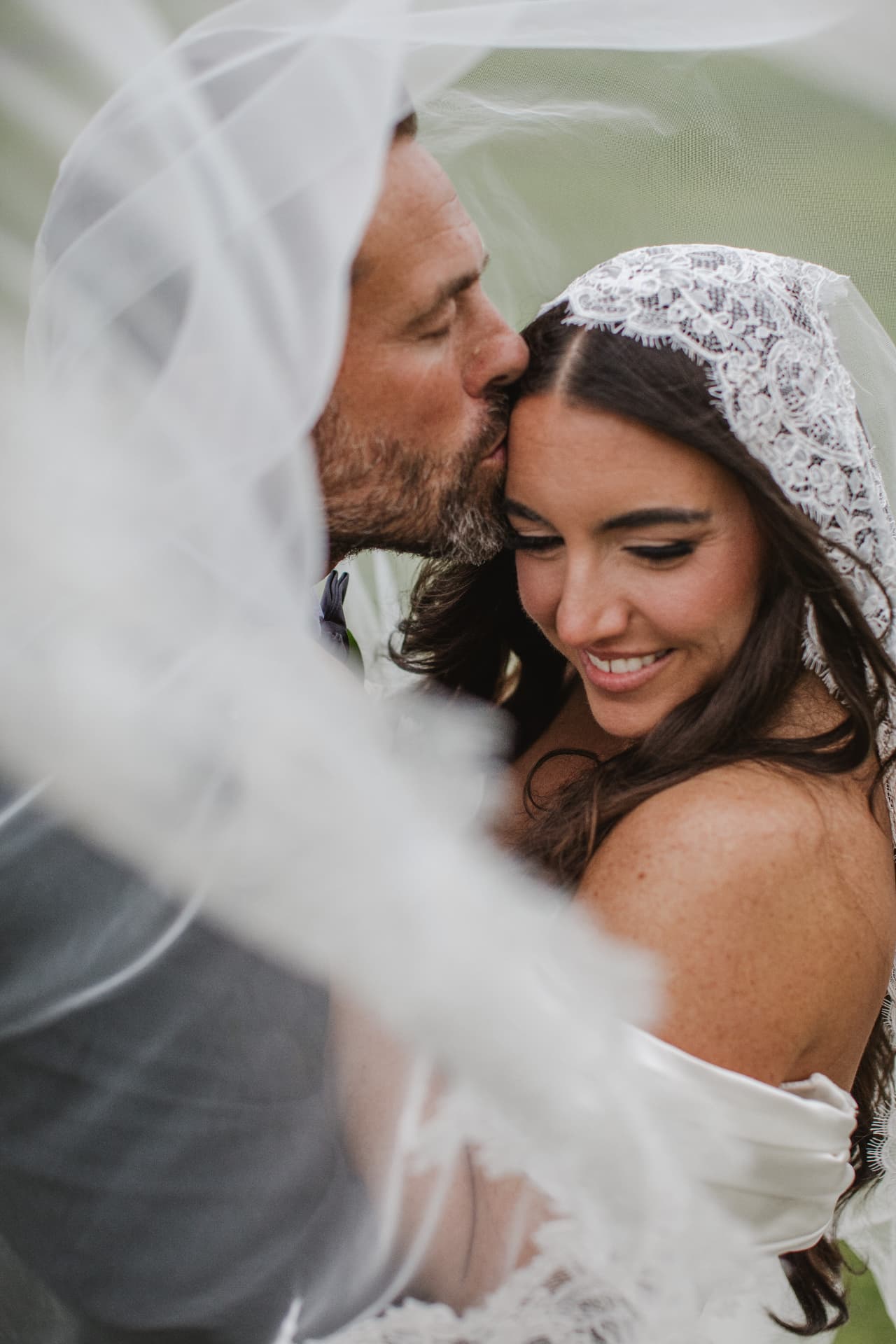 Groom kissing his bride's forehead beneath her flowing veil